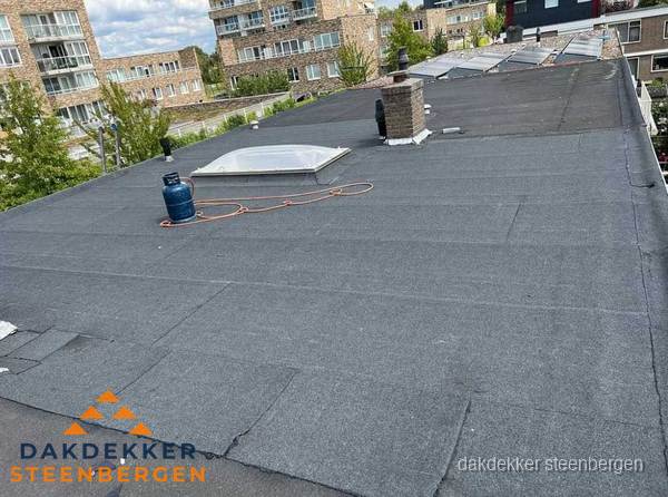 Bitumen dakbedekking op plat dak met lichtkoepel en schoorsteen in Steenbergen