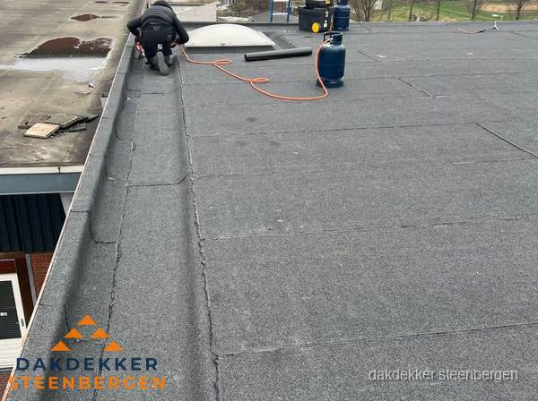 Dakdekker repareert bitumen dakbedekking op groot plat dak in Steenbergen